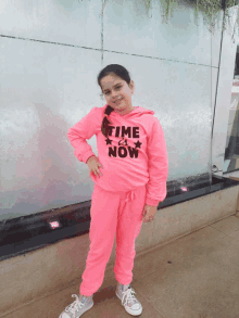 a little girl wearing a pink hoodie that says time & now