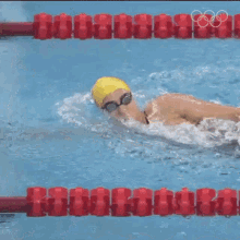 a woman in a yellow swim cap and goggles is swimming in a pool with the olympic rings in the background