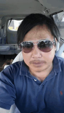 a man wearing sunglasses and a blue polo shirt takes a selfie in a car