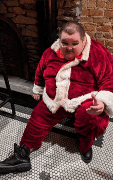 a man in a santa suit sits on a tiled floor and gives a thumbs up