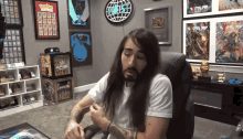 a man with long hair sits in a chair in front of a wall that has a sign that says " world "