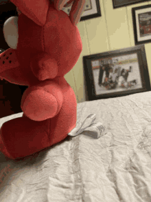 a red stuffed animal sits on a bed in front of a framed hockey picture