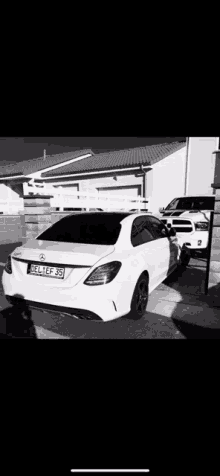 a white mercedes benz is parked in front of a house in a parking lot .