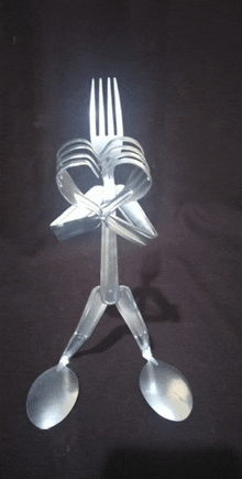 a person made out of plastic forks and spoons on a black surface