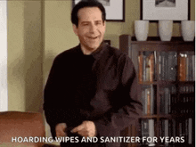 a man in a black shirt and tie is standing in a living room with a bookshelf in the background .