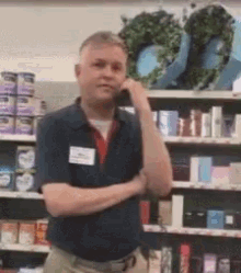 a man in a blue shirt with a name tag on his neck is standing in front of a store shelf