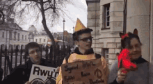 a group of people are standing in front of a building holding signs . one of the people is wearing a yellow hat .