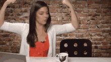 a woman is flexing her muscles in front of a brick wall while sitting at a desk with a laptop .