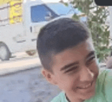 a young boy in a green shirt is smiling in front of a white truck .