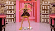 a drag queen is standing in a room with mannequins and a sign that says dead .