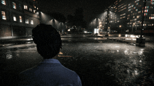 a person standing in a parking lot at night with buildings in the background