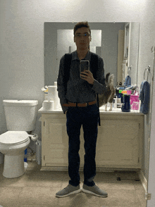 a man takes a selfie in a bathroom with a cat behind him