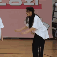 a woman in a white shirt and black pants is standing on a basketball court with her arms outstretched .