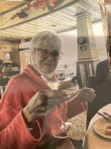 a woman in a red sweater is holding a martini in a restaurant