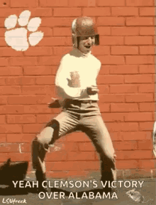 a man in a football helmet is dancing in front of a brick wall with a clemson logo on it .