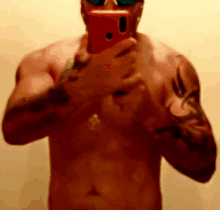 a shirtless man is taking a picture of himself with a red cell phone .