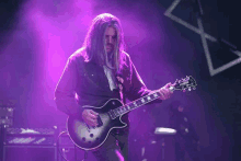 a man with long hair is playing a guitar in front of purple lights