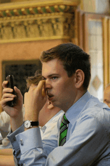 a man in a blue shirt and green tie is looking at his cell phone