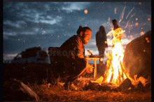 a man is kneeling in front of a fire at night