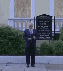 a man in a suit and tie is standing on a sidewalk in front of a building holding a sign .