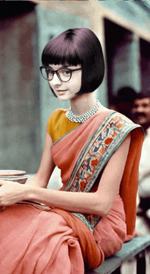 a woman wearing glasses and a pink saree is sitting on a bench