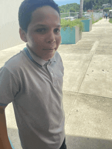 a young boy wearing a grey shirt stands on a sidewalk