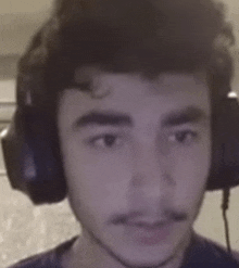 a young man wearing headphones and a mustache is looking at the camera .