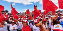 a crowd of people holding up red flags and wearing hats that say " frente "