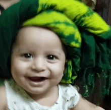 a baby wearing a green and yellow scarf on his head smiles