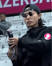 a woman is holding a gun in a stadium while wearing glasses .