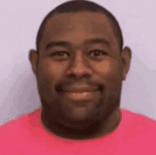 a man in a pink t-shirt is smiling for the camera .