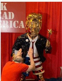 a man in a red shirt is touching a statue of trump