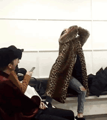 a woman in a leopard print coat is sitting in a waiting room with other people .