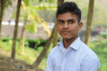 a young man in a blue and white striped shirt looks at the camera