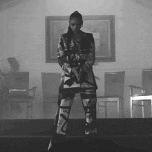 a black and white photo of a woman standing in a room with chairs and a picture on the wall