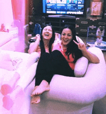 two women are sitting on a bean bag chair in front of a television .