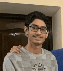 a young man wearing glasses and a shirt that says attitude smiles for the camera