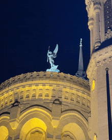 a statue of an angel holding a sword on top of a building at night