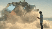 a boy is holding a remote control while standing in front of a pile of rubble on a beach .