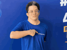 a man wearing glasses and a blue shirt that says pagaemem points at his chest