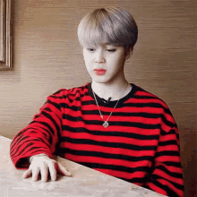 a young man wearing a red and black striped shirt is sitting at a table with his hand on the table .