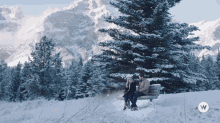 a man and a woman sit on a bench in the snow with the letter w on the bottom left