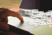 a person 's finger is pointing at a laptop keyboard with envelopes coming out of it