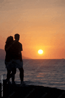 a silhouette of a man and woman standing on a beach watching the sun set over the ocean