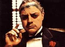 a man in a tuxedo is smoking a cigar and looking at the camera .