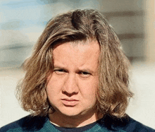 a man with long hair is wearing a blue shirt and making a funny face