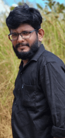 a man wearing glasses and a black shirt stands in a field of tall grass