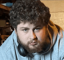 a man with curly hair and a beard wearing headphones and a hoodie .