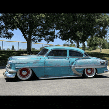 a blue car with white tires is parked in front of a baseball field