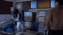 a man and a woman are standing in front of a stack of cardboard boxes labeled fake flowers & candles